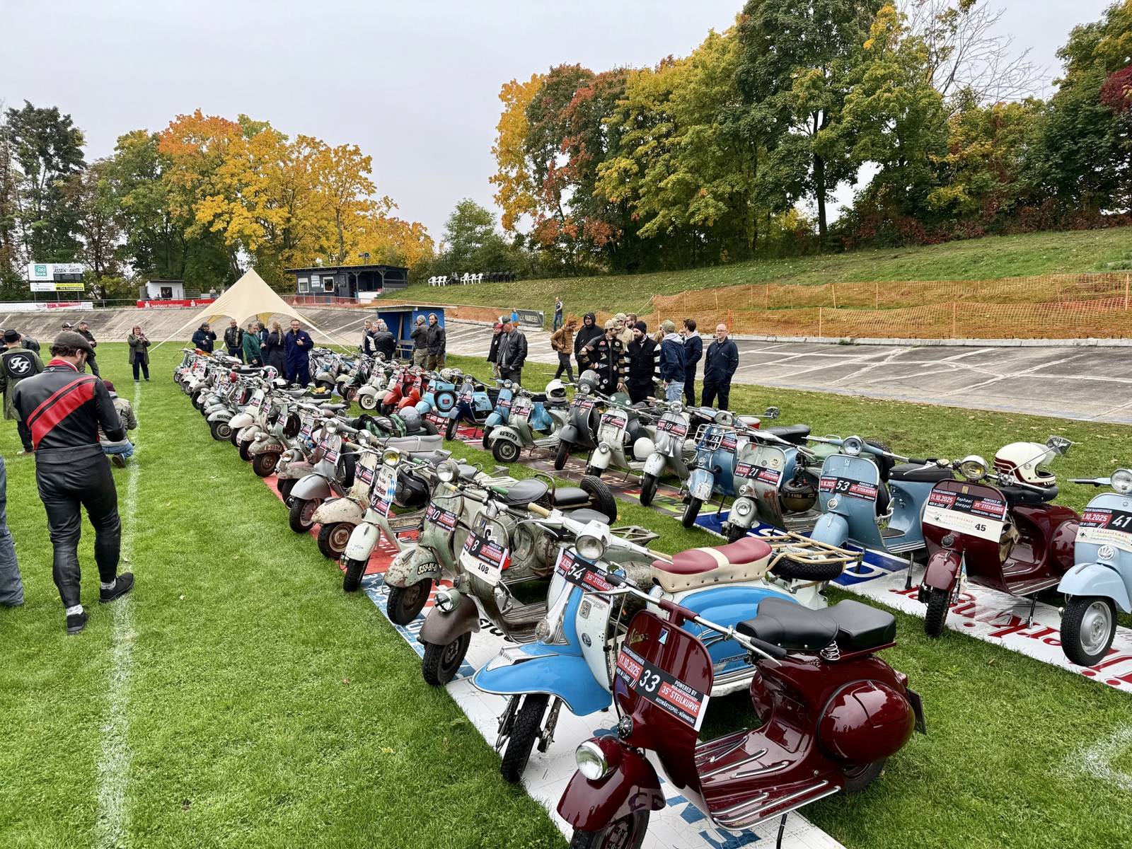 Lange Reihe klassischer Vespas mit Startnummern im Innenraum der Radrennbahn